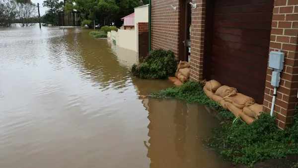 Sandbags lined up against a brick garage during a street flood